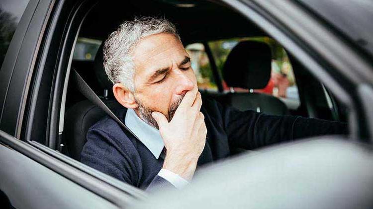 Man yawning at the wheel of a car trying not to fall asleep.