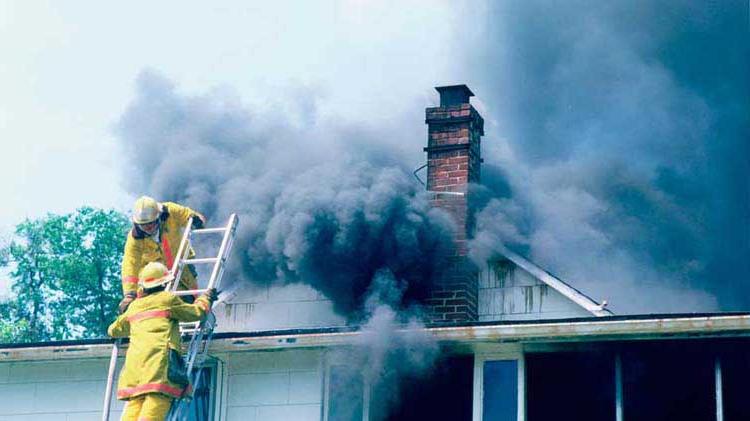 消防队员站在梯子顶端，准备扑灭一场屋顶冒出黑烟的房屋火灾.