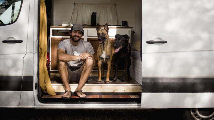 一个面带微笑的男人和他的狗坐在一辆房车里