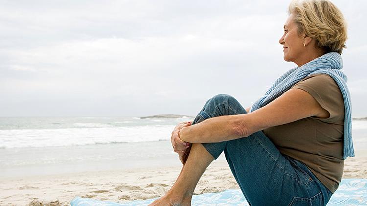一个女人坐在沙滩上的毯子上，看着外面的水.