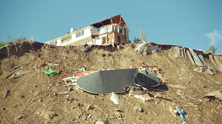 A house damaged by an earthquake sits atop a hill that is covered in debris.
