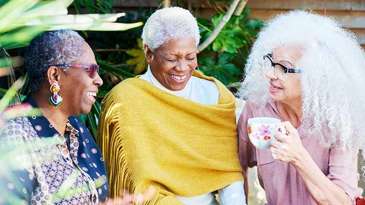 三个女人笑着谈论她们的退休生活，坐在外面喝咖啡.